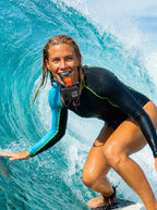A smiling female surfer in a wetsuit using the Azragon Pro Bite Mount with a GoPro camera and a dual security neck lanyard to shoot professional surf POV videos.